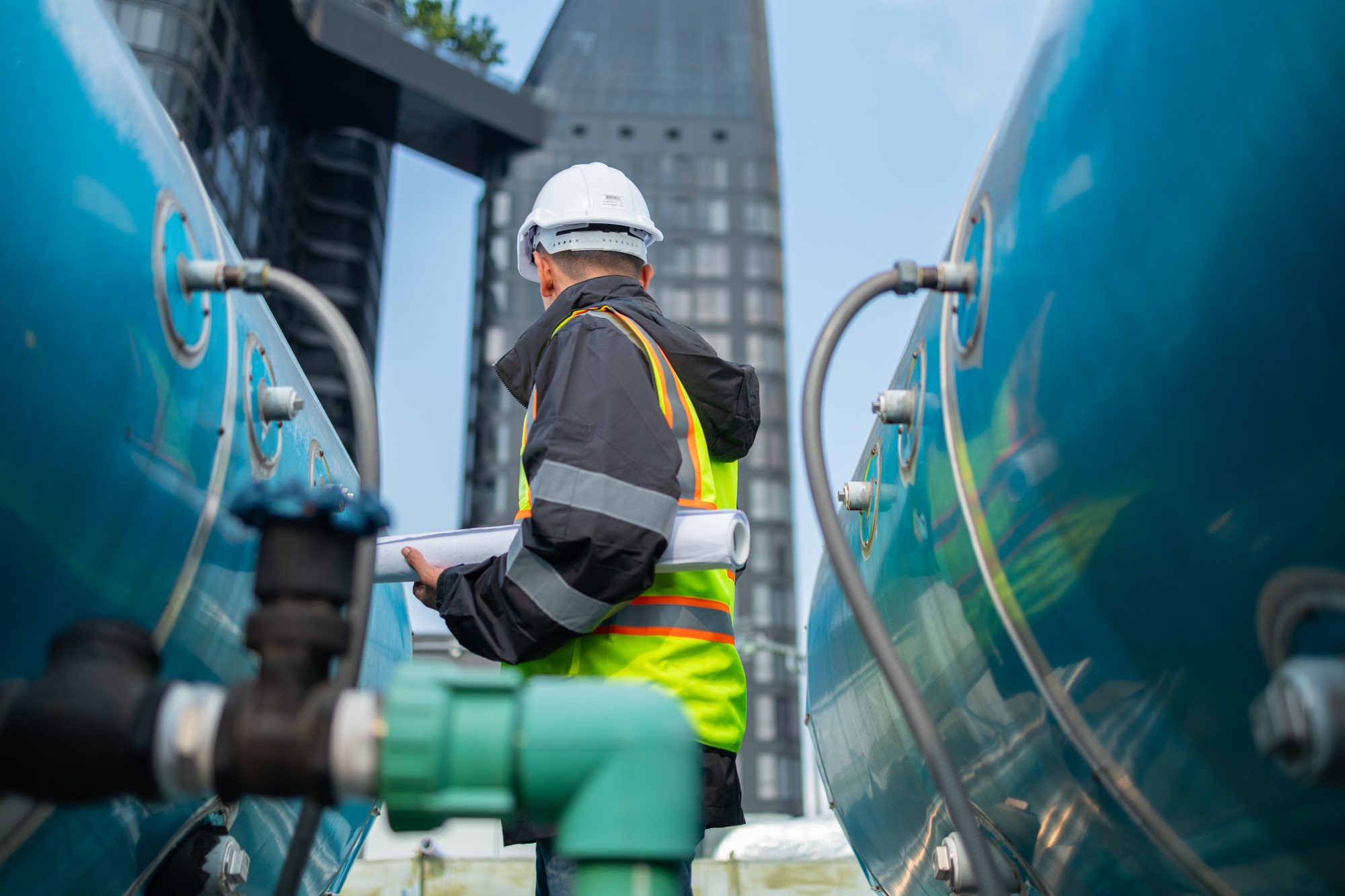 Engineer inspects water heater pump system and hot water tank on industrial roof